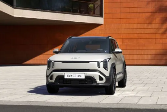 Vista frontal del Kia EV2 GT-Line color marfil, un SUV eléctrico compacto estacionado frente a un edificio moderno con paneles de madera