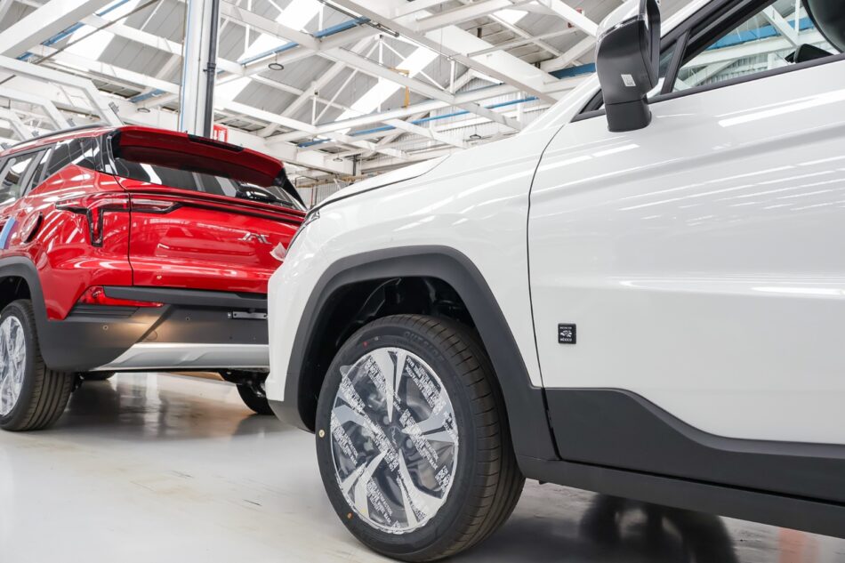 JAC México integrará sello Hecho en México en toda su línea 2027 Memo Lira Camioneta blanca en una sala de exposición rueda en primer plano con cubierta protectora y embellecedor de guardabarros negro SUV rojo al fondo