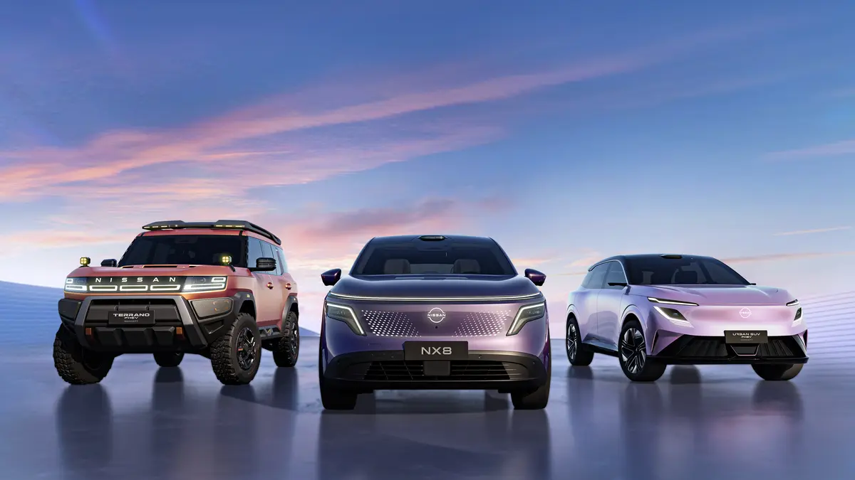 Three Nissan vehicles parked on a reflective surface at sunset: a rugged orange off-roader left, a silver NX8 center, and a lavender urban SUV on the right.