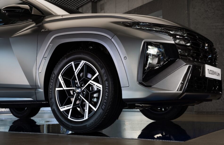 Hyundai Tucson Híbrida N Line 2026 lateral Memo Lira Primer plano de la sección delantera izquierda de un SUV gris metalizado donde se aprecian una elegante llanta de aleación multirradio un llamativo grupo óptico y el emblema N Line