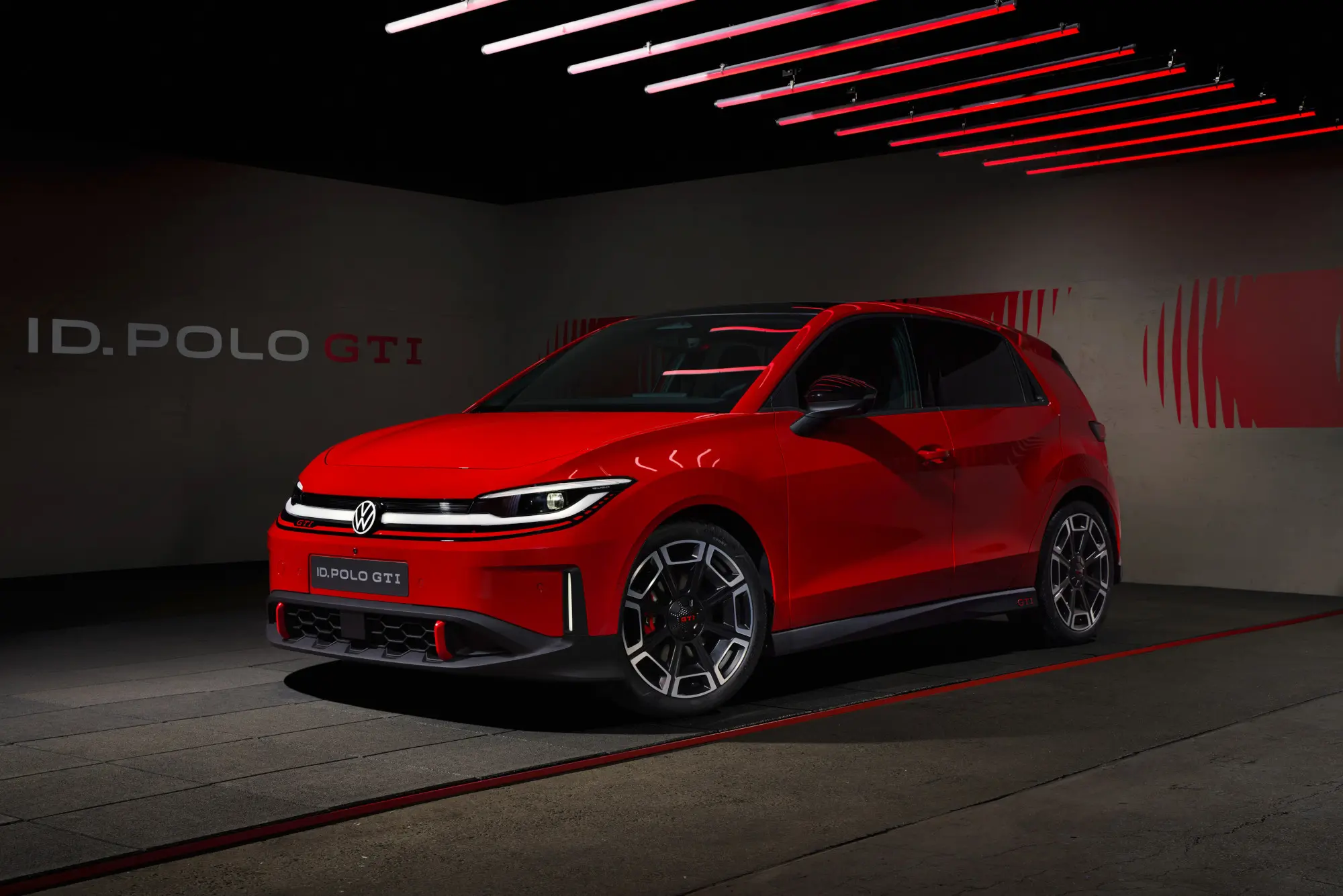 Red Volkswagen ID. Polo GTI on display in a dark showroom with red neon light bars overhead.
