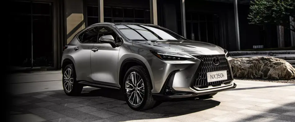 NX350Hybrid Memo Lira Vista frontal de tres cuartos de un SUV Lexus NX350h plateado estacionado en una zona pavimentada con piedra frente a un edificio moderno