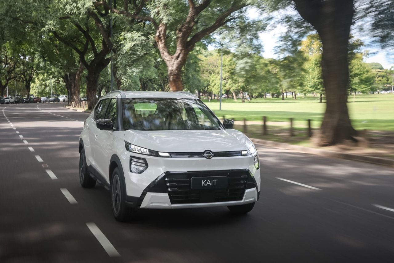 Vista frontal de Nissan KAIT SUV blanco circulando por una calle arbolada con un parque a la derecha.
