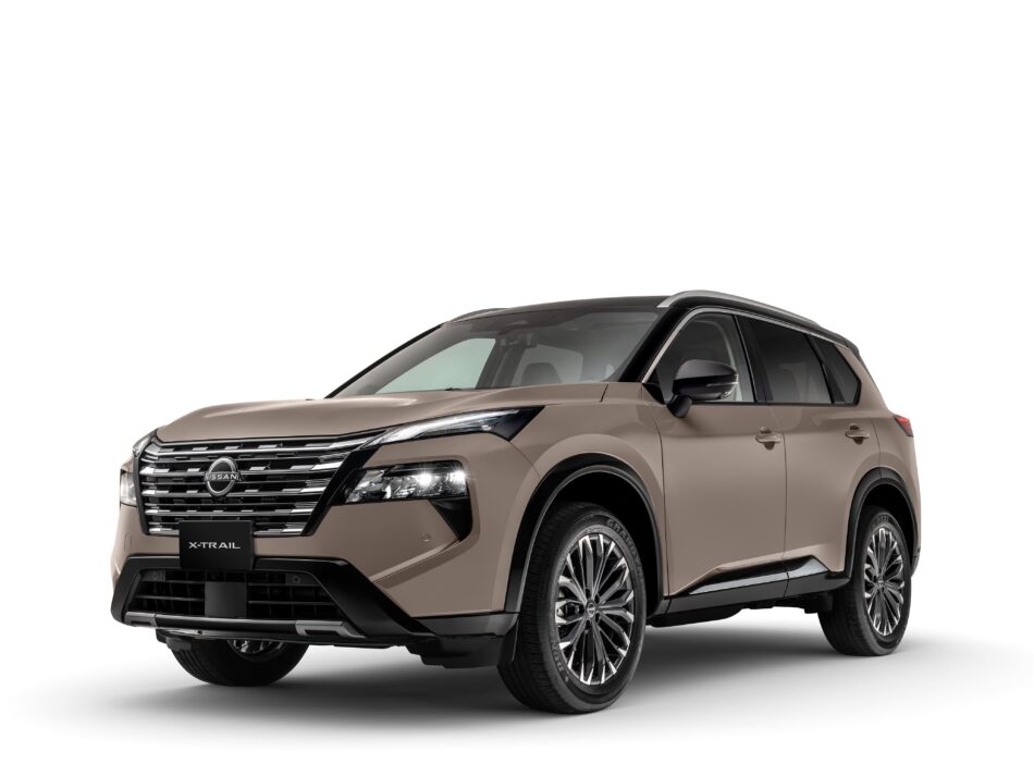 Vista de la esquina delantera izquierda de un SUV Nissan X-Trail de color beige, en la que se aprecian la parrilla cromada y el emblema de Nissan sobre ella.