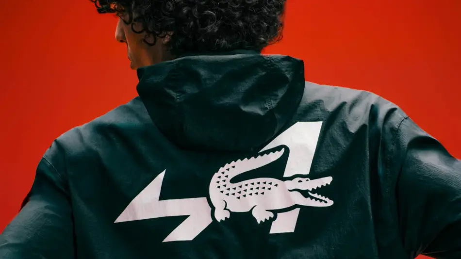 Back view of a person wearing a dark hooded jacket with a large white crocodile logo and zigzag shapes on the back against a red background