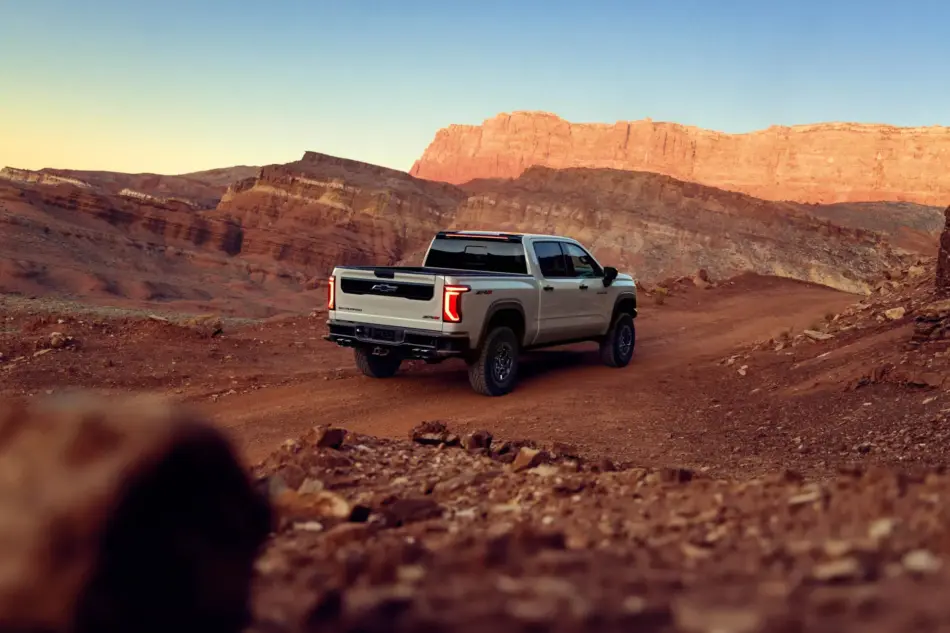 MY27 ChevroletSilveradoZR2Rear Driving Memo Lira White Chevy Silverado pickup parked on a dusty desert road with red canyon walls at sunset