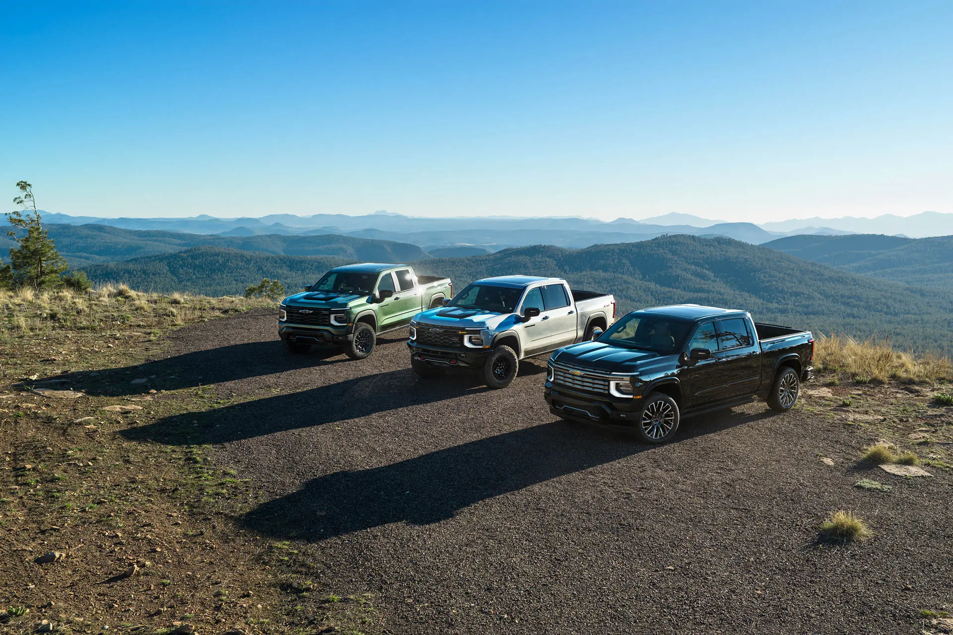 Tres camionetas aparcadas en un mirador rocoso, con una extensa cordillera y un cielo azul al fondo, que muestran un paisaje natural y agreste.