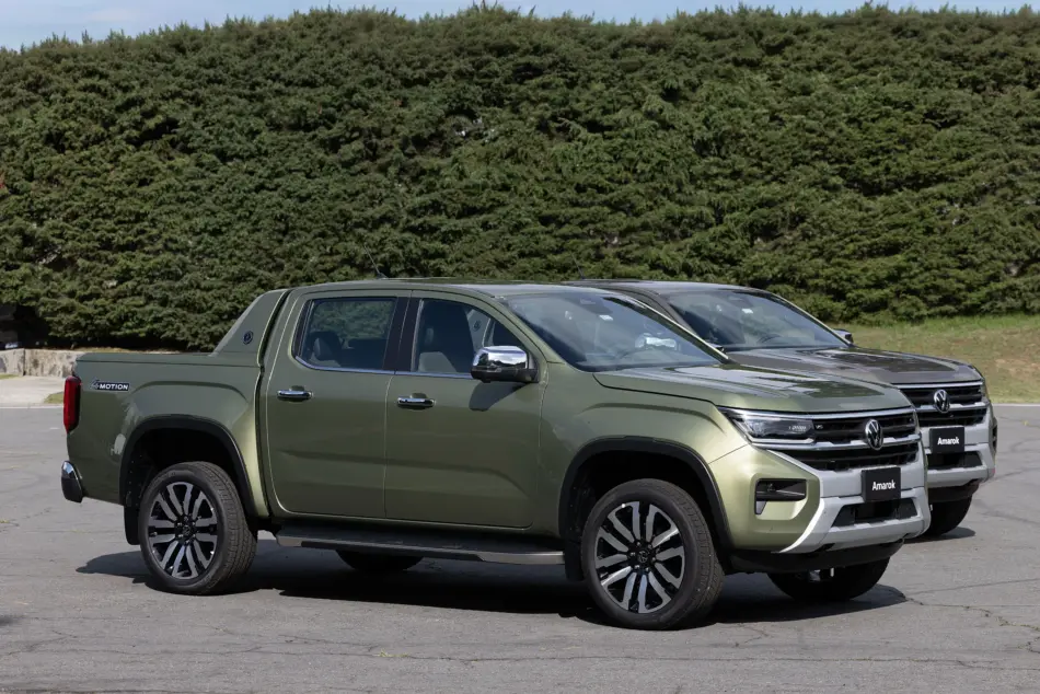 Volkswagen Amarok 2026 diferentes versiones Diseño exterior Memo Lira Two green Volkswagen Amarok pickup trucks parked side by side in a lot with a dense hedge behind them