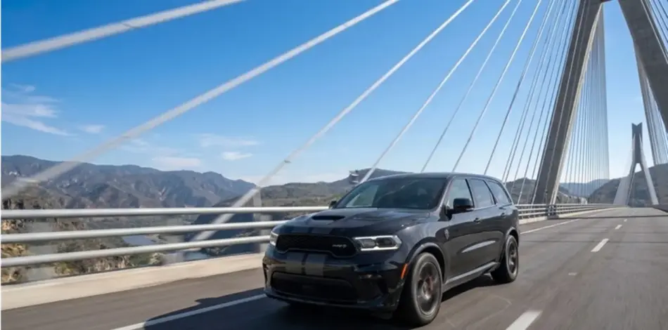 Dodge Durango Hellcat Black Demon 2 Memo Lira Black SUV driving on a modern cablestayed bridge with mountain landscape in the background