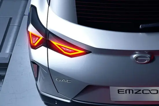 Vista trasera de un coche GAC Emzoom de color plateado con unas distintivas luces traseras rojas de formas angulares que se iluminan contra el borde de una superficie gris.