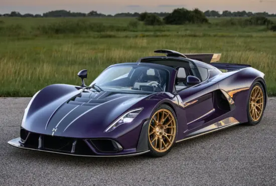 Purple convertible sports car with gold wheels on a paved road, open cockpit, field backdrop at sunset.