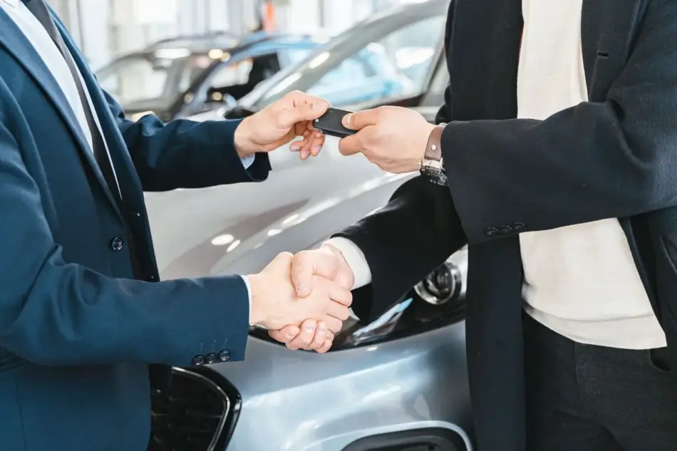 Dos profesionales se dan la mano mientras se entregan las llaves de un coche en la sala de exposición de un concesionario