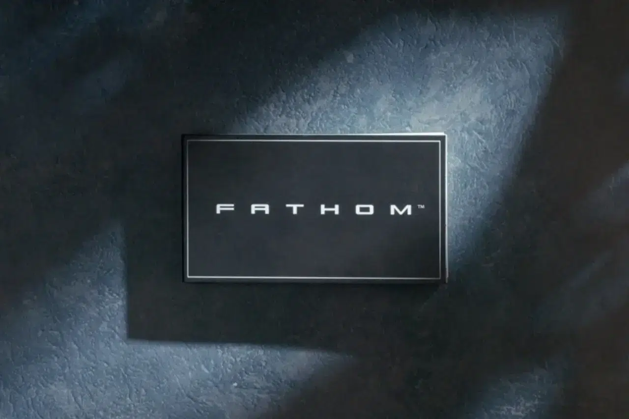 Un panel negro enmarcado sobre una pared oscura con textura, en el que se lee la palabra «FATHOM» en blanco en el centro.