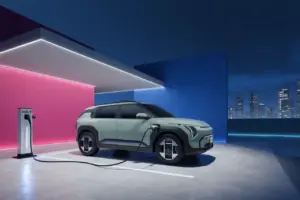 Un SUV eléctrico recargándose por la noche en una estación futurista situada en una azotea, con paredes de color rosa y azul, y el perfil de la ciudad al fondo.