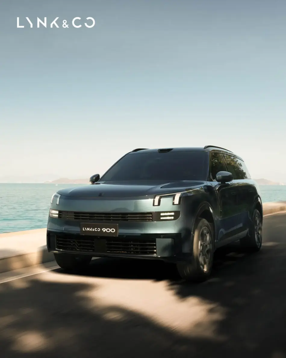 Lynk Co 900 el nuevo rostro del lujo automotriz Memo Lira Vista frontal en ángulo de un SUV Lynk Co 900 de color azul oscuro circulando por una carretera costera con el mar a la izquierda y un cielo despejado por encima logotipo en la esquina superior izquierda