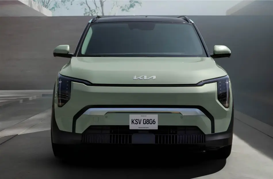 Vista frontal de un SUV Kia EV3 de color verde claro con una parrilla llamativa y faros estrechos aparcado en el interior de una sala de exposición