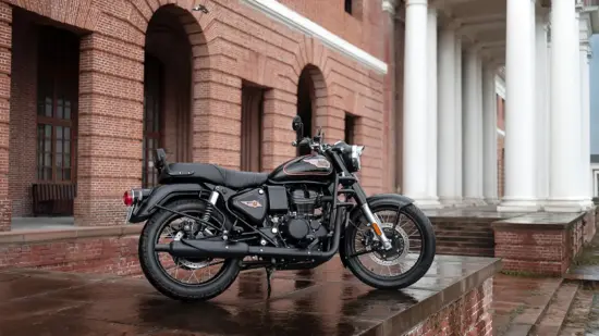 Black Royal Enfield Bullet motorcycle parked on wet brick steps beside a red brick building with arches and a white-columned portico.